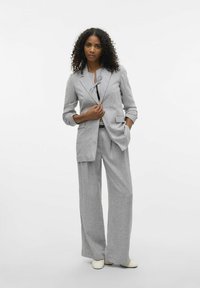 Blazer gris ajustado y pantalones de pierna ancha hechos de una tela texturizada. Cuenta con un cierre de un solo botón y bolsillos abiertos.