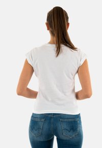 T-shirt bianco in cotone con maniche arrotolate, abbinato a jeans in denim blu con tasche posteriori caratterizzate da un motivo a zigzag.