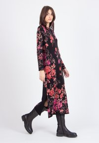 Black floral dress with long sleeves, featuring red and pink flower patterns, side slits, and paired with knee-length black boots.
