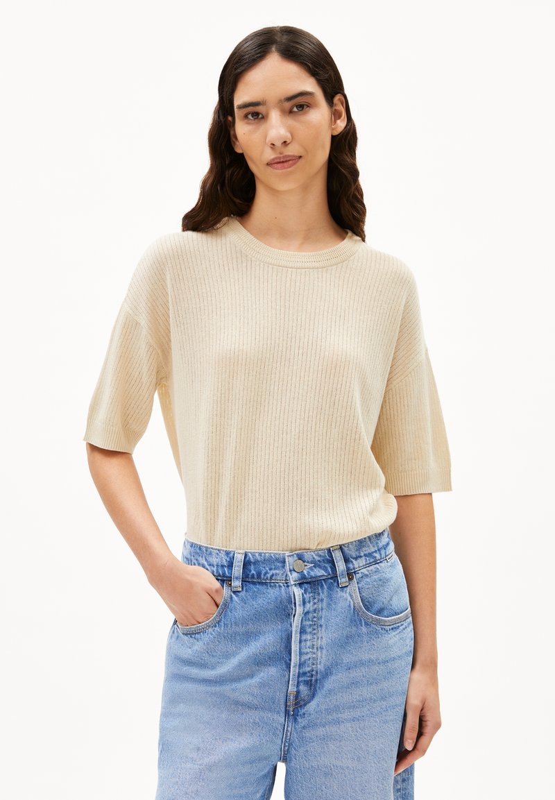 Helles beige, geripptes Kurzarmpullover mit Rundhalsausschnitt, kombiniert mit hochtaillierten, hellblauen Jeans. Lockere Passform und glatte Textur.