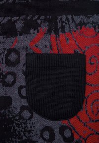 Svart stickad ficka i ett mönstrat tyg med abstrakta röda och grå cirkulära och virvlande mönster.