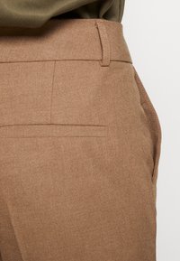 Brown fabric trousers featuring a smooth texture, clean lines, and a back pocket with a stitched edge. Minimalist design and tailored shape.