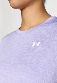 Gaiši violets sporta krekls ar apaļu apkakli, īsām piedurknēm un mazu baltu logo uz krūšu daļas. Mīksta, teksturēta auduma.