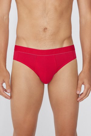 Torso masculino con ropa interior tipo slip de color rojo sólido, de pie contra un fondo sencillo.