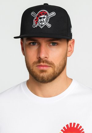 Black baseball cap with embroidered pirate graphic, featuring a red bandana and crossed bats. Worn with a plain white shirt.