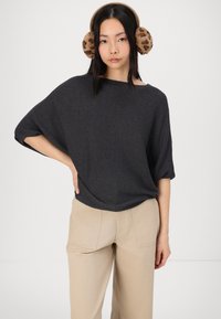 Grå, teksturert oversized skjorte med vide ermer, kombinert med lyse beige bukser. Modellen har også på seg brune ørevarmere med dyreprint.