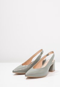 Slingback podpatky z jemné šedé kůže, špičaté, s malým blokovým podpatkem a elastickým popruhem pro bezpečné nošení. Hladký povrch.