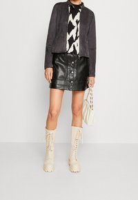 Minigonna nera in pelle con bottoni frontali, abbinata a una giacca grigia testurizzata e un maglione a motivo; stivali beige con lacci fino al ginocchio.