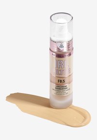 Fond de teint longue tenue dans un flacon clair avec un applicateur pompe, arborant une étiquette dorée et rose. Teinte F8.5, avec un échantillon de liquide beige clair à côté.