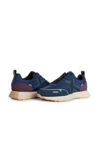 Scarpe sportive blu navy con una miscela di materiali testurizzati, dotate di una tomaia in mesh blu scuro, dettagli in suede viola e una suola in gomma beige.