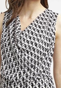 Svartvitt ärmlöst klänning med ett sjöhästmönster, med draperad tyg på bodice och mjuk, slät textur.