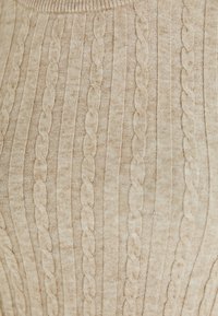 Tissu tricoté beige avec motifs torsadés verticaux et côtes créant des lignes parallèles texturées.