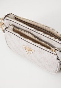 Beige Handtasche mit strukturiertem Material und zwei Reißverschlussfächern, goldener Hardware und einem dreieckigen Logo-Akzent. Verfügt über einen abnehmbaren Trageriemen.