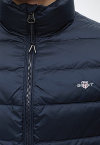 Veste matelassée bleu marine avec une fermeture éclair à l'avant et un petit logo GANT brodé sur le côté droit de la poitrine.