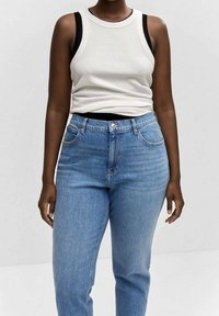 Camiseta sin mangas blanca acanalada con ribete negro combinada con vaqueros de tiro alto en azul claro. Los vaqueros presentan un estilo clásico de cinco bolsillos y cierre de botón.