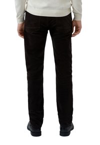 Brown corduroy trousers feature a slim fit and two back pockets. Worn with black shoes and a light-colored sweater.