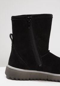 Černé semišové kozačky do poloviny lýtek se zipem na boku, poutkem na patě a silnou šedou gumovou podrážkou s vroubkovaným dezénem.