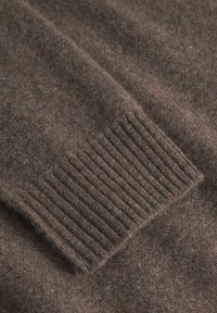 Brauner Wollpullover-Stoff mit einem gerippten Bündchen. Die Textur ist weich und zeigt eine subtile Variation in Farbe und Licht.