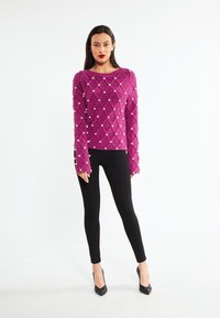 Fuchsia strikket sweater med diamantmønster og perleindslag, parret med sorte leggings og spidse sorte hæle. Tekstureret materiale.