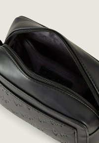 Borsa a tracolla in pelle nera con texture liscia, chiusura con zip e dettagli in rilievo sulla parte anteriore. Interno foderato in tessuto scuro.
