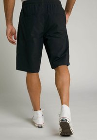 Schwarze Shorts mit einem elastischen Bund, seitlichen Taschen und einer lockeren Passform, kombiniert mit weißen High-Top-Sneakern. Glatte Stofftextur.