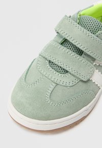 Roheline seemisnahast toss võrkdetailidega, kahepoolsete Velcro rihmade, valge õmbluse ja tekstuurse kummist tallaga. Omaduseks ümar varbaosa disain.