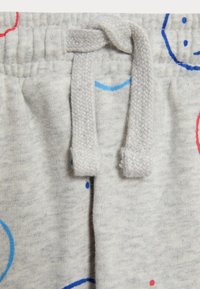 Helle graue Jogginghose mit einem Kordelzugbund, verziert mit bunten Smiley-Gesichtsmustern in Blau, Rot und verschiedenen Formen auf dem Stoff.