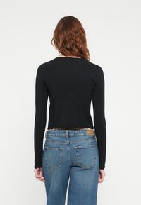Top negru cu maneci lungi, cu un design scurtat și margine zimțată, purtat cu blugi deschiși la culoare, cu talie înaltă și buzunare clasice la spate.