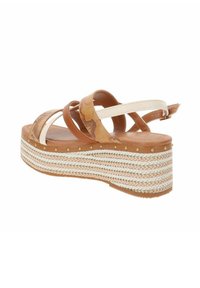 Sandales à talon compensé marron et beige avec une plateforme en jute tressé, présentant des brides croisées et une boucle à l'arrière. Des clous dorés discrets accentuent la semelle.