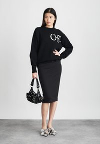 Zwarte gebreide trui met "Off" tekst, gecombineerd met een zwarte getailleerde rok. Geaccessoriseerd met een zwarte handtas met studs en grijze versierde schoenen.