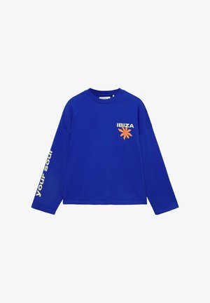 Kék hosszú ujjú ing "IBIZA" felirattal és narancssárga virággal az elején, valamint krémszínű "your soul" felirattal a bal ujjon.