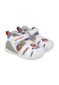 Sandalias blancas para niños con recortes, correa de velcro, acentos grises y diseños coloridos de piratas en los costados. Suela de goma para mayor agarre.