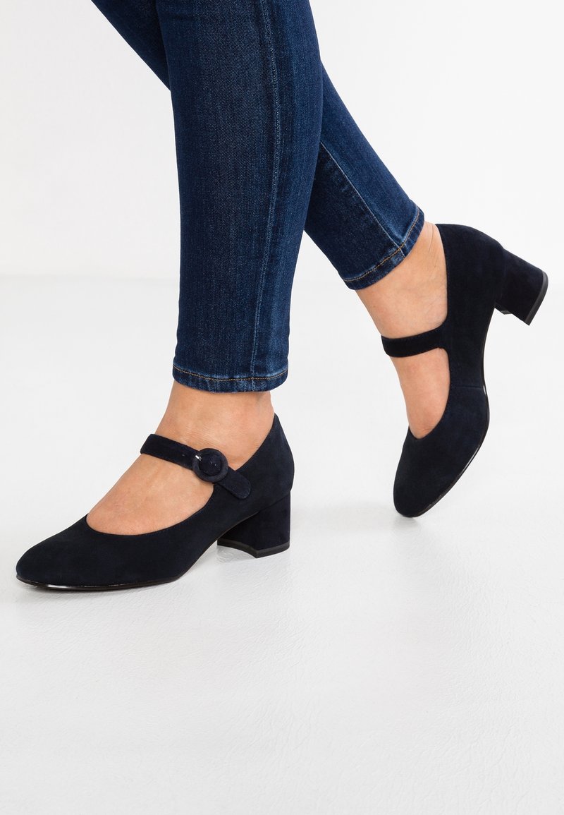 Femme portant des chaussures Mary Jane en daim bleu marine avec une boucle ronde et des talons blocs, associées à un jean skinny bleu marine.