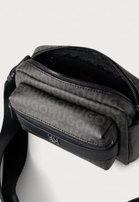 Mala tiracolo preta e cinzenta texturizada com vários compartimentos com fecho éclair, apresentando um design elegante e detalhes metálicos contrastantes.