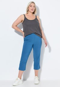 Top sin mangas gris combinado con pantalones cortos turquesa, con una textura de tela suave y aberturas laterales en el dobladillo. Zapatillas blancas completan el look.