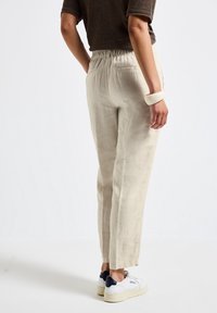 Ljust beige linnebyxor med avslappnad passform, elastisk midja och avsmalnande ben, som är kombinerade med vita sneakers med marinblå accenter.