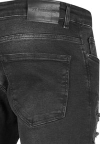 Czarne dżinsy denimowe o zużytej fakturze, z skórzaną metką, tylnymi kieszeniami i przetartymi detalami na końcach.