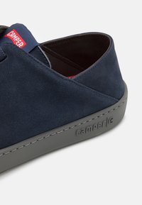 Scarpa in suede blu con suola in gomma grigia. Presenta un logo Camper su un'etichetta blu, dettagli cuciti e un rivestimento interno testurizzato.