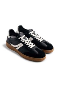 Zapatillas de deporte en blanco y negro, hechas de cuero y gamuza, con una suela de goma, cordones blancos y rayas laterales texturizadas.