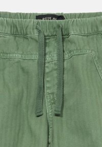 Grüne Shorts mit Fischgrätmuster, elastischem Bund und Kordelzug. Der Stoff ist glatt und leicht und verfügt über seitliche Taschen.
