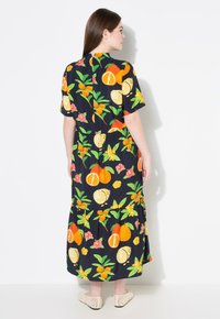 Vestido negro con un patrón de frutas y flores coloridas, mangas cortas, falda de volantes y tejido ligero. Presenta vibrantes acentos en naranja y amarillo.