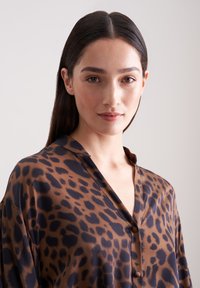 Blusa con stampa leopardata marrone e nera, dotata di colletto, bottoni frontali e una texture leggera e liscia. Progettata con una vestibilità rilassata.