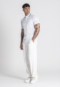 Biela polokošeľa s jemným vzorom, kontrastným golierom, v kombinácii s voľnými bielymi nohavicami a svetlými teniskami.