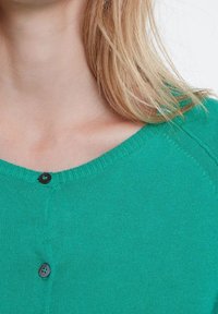 Grüner Strickcardigan mit Rundhalsausschnitt, der eine strukturierte Oberfläche und einen schwarzen Knopf in der Mitte vorne zur VerschClosure hat.