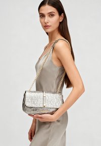 Borsa in pelle argentata con motivo in rilievo, dettagli in oro e tracolla a catena. Presenta una chiusura a patta e dettaglio con logo.