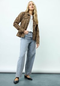 Giacca di jeans con stampa leopardata, jeans a vita alta azzurri chiari e ballerine nere. Texture liscia, vestibilità strutturata e dettagli accentuati sottili.