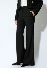 Pantaloni neri a gamba larga in un tessuto liscio con cuciture sartoriali e tasche laterali, abbinati a una giacca cropped nera di tessuto testurizzato.
