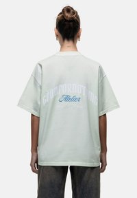 T-shirt oversized verde chiaro con maniche corte. Presenta "GOODFORNOTHING" in bianco e "Atelier" in blu sul retro. Tessuto di cotone morbido.