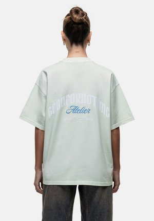Lichtgroene oversized t-shirt met korte mouwen. Heeft "GOODFORNOTHING" in het wit en "Atelier" in het blauw op de achterkant. Zachte katoentextuur.