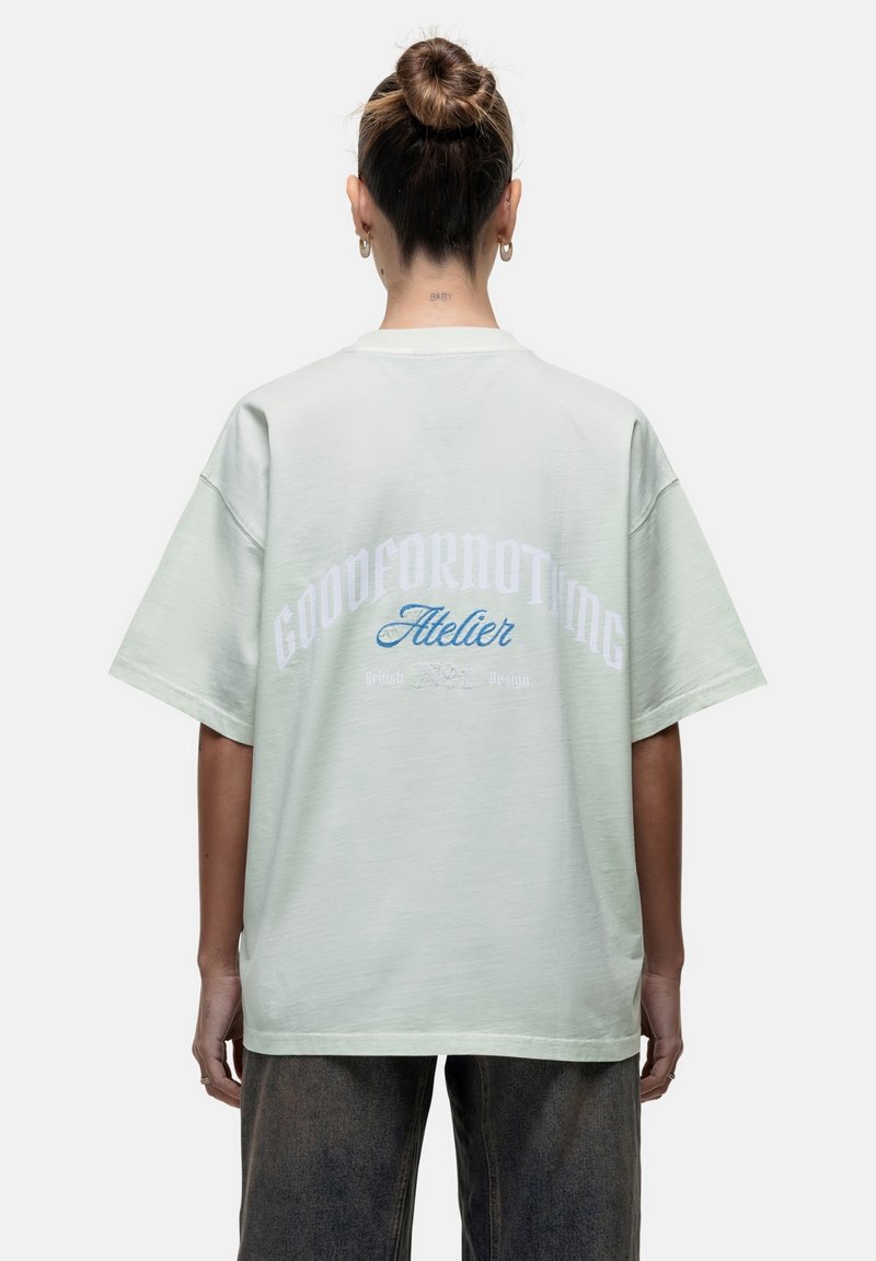 T-shirt oversized verde chiaro con maniche corte. Presenta "GOODFORNOTHING" in bianco e "Atelier" in blu sul retro. Tessuto di cotone morbido.
